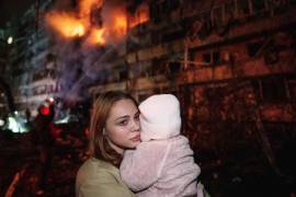 Victoria Deineko sostiene a su hija Mia frente a un edificio residencial dañado por un ataque con misiles rusos en Kiev, el 13 de octubre de 2026.