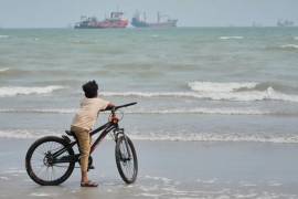 Un niño está de pie con su bicicleta en una playa con vistas a los buques mercantes anclados en el estrecho de Ormuz, frente a Bandar Abbas, Irán.