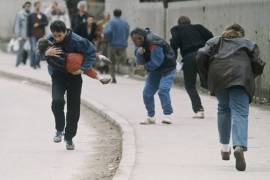 Un hombre acuna a su hijo mientras la gente pasa corriendo por uno de los peores lugares para los francotiradores en Sarajevo en abril de 1993.
