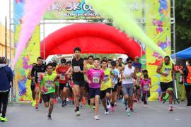 Participantes cubiertos de color cruzan la línea de meta en un ambiente de alegría.