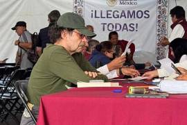 La imagen muestra a un Quadri cabizbajo, con una playera y gorra verde olivo y una sudadera gris amarrada en la cintura, con los brazos cruzados sobre la mesa, mientras espera ser atendido.