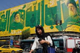 Una mujer cruza una intersección frente a una valla publicitaria que muestra retratos del difunto líder supremo iraní, el ayatolá Ali Khamenei (derecha), los difuntos líderes del grupo Hezbolá del Líbano, Hassan Nasrallah (centro izquierda) y Hashem Safieddine.