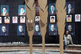 Un hombre iraní está sentado bajo un muro decorado con imágenes de líderes iraníes y de personas fallecidas en la guerra, incluidos niños de Minab, en las calles de Teherán, la capital de Irán.