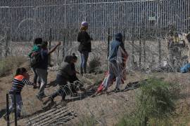 Migrantes esperan entre los alambres de púas mientras un agente estadounidense vigila, el 26 de mayo de 2024 en Ciudad Juárez, Chihuahua (México).