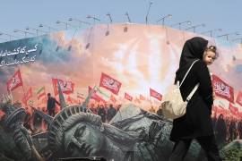 Una mujer iraní que lleva a su hijo en brazos pasa junto a una valla publicitaria antiestadounidense en la plaza Enghelab, en el centro de Teherán, Irán, el 3 de agosto de 2026.