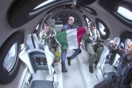 El coronel Walter Villadei, de la Fuerza Aérea italiana, sostiene una bandera de su país acompañado por otros investigadores italianos en una nave de Virgin Galactic, antes de regresar a Nuevo México.