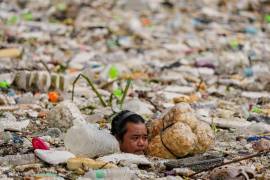 Un trabajador con flotadores improvisados intenta despejar un mar de basura y escombros arrastrados por las intensas lluvias del monzón en el canal de drenaje Redentorista, enParañaque, Gran Manila, Filipinas.