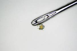 El pequeño cangrejo robótico junto al ojo de una aguja de coser.