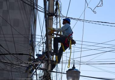 Trabajadores de CFE laboran en lo alto de un poste de la compañía.