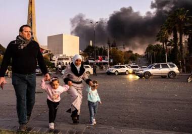 Una familia llega para celebrar la caída del gobierno sirio con humo de fondo en Damasco, Siria, el 8 de diciembre de 2024.