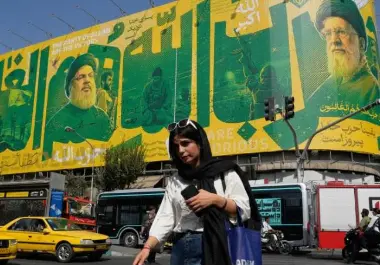 Una mujer cruza una intersección frente a una valla publicitaria que muestra retratos del difunto líder supremo iraní, el ayatolá Ali Khamenei (derecha), los difuntos líderes del grupo Hezbolá del Líbano, Hassan Nasrallah (centro izquierda) y Hashem Safieddine.