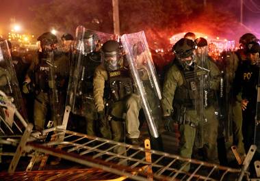 Policías derriban una barricada durante un enfrentamiento con manifestantes cerca del centro de detención Delaney Hall, durante una protesta contra el traslado de detenidos y las políticas federales de inmigración.