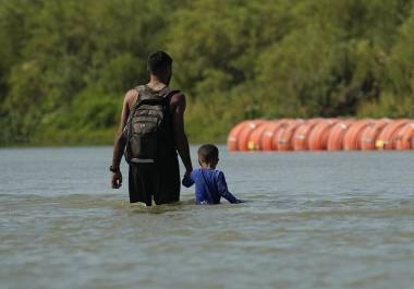 Migrantes pasan junto a grandes boyas que se utilizan como barrera fronteriza flotante en el Río Grande, el 1 de agosto de 2023, en Eagle Pass, Texas.