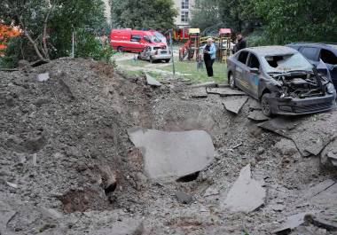Residentes locales permanecen cerca de un cráter y de automóviles dañados por un ataque con misiles rusos en Kiev, Ucrania, el lunes 6 de julio de 2026. (Foto AP/Efrem Lukatsky)