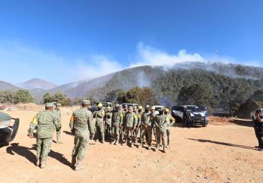 Brigadistas luchando contra el incendio en El Tunal, Arteaga, mientras helicópteros realizan descargas de agua sobre la zona afectada.