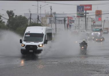 Autos atravesando una calle afectada por inundaciones, destacando la importancia de evitar conducir por áreas con agua estancada para prevenir accidentes y daños a los vehículos.