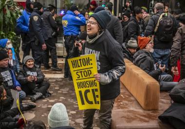 Una activista sostiene un cartel en el vestíbulo de un hotel con el mensaje: “Hilton: dejen de alojar al ICE”, reflejando la toma de espacios privados para la protesta.