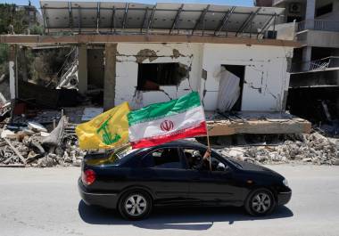 Residentes desplazados portan banderas de Irán y Hezbolá al pasar junto a un edificio destruido que fue alcanzado por un ataque aéreo israelí en la aldea sureña de Chehabiyeh, Líbano.