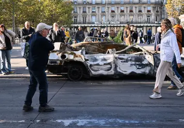 Gente mira a un auto calcinado en Place de la Republique el día después de una manifestación contra el creciente coste de la vida, que se suma a las protestas estudiantiles, en París.