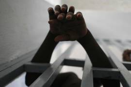 Joven prisionero saca sus manos a través de los barrotes de una cárcel