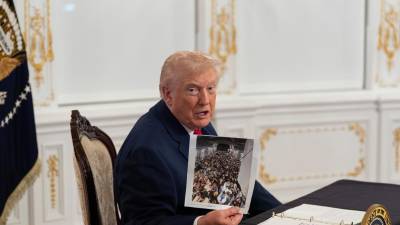 El presidente Donald Trump sostiene una fotografía mientras se dirige a reporteros tras hablar con las tropas por video desde su residencia de Mar-a-Lago en Palm Beach, Florida. FOTO: AP / Alex Brandon