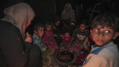 Amani Abu Zarada, cuarta por la izquierda, alimenta a uno de sus hijos con calabacines fritos hechos sobre un fuego hecho con restos de papel y cartón fuera de su tienda de campaña en un campamento de Jan Yunis, Franja de Gaza.