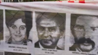 Oficiales del ejército observan desde el interior de la base militar de Campo de Mayo mientras los manifestantes sostienen una pancarta cubierta de imágenes de víctimas de la dictadura militar argentina.