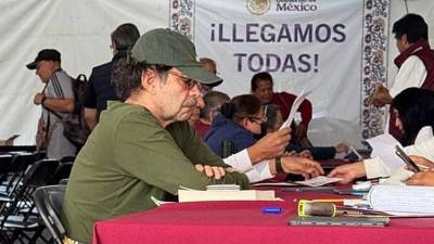 La imagen muestra a un Quadri cabizbajo, con una playera y gorra verde olivo y una sudadera gris amarrada en la cintura, con los brazos cruzados sobre la mesa, mientras espera ser atendido.