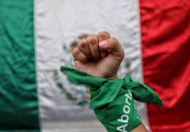 En la imagen una mujer posa con pañuelo verde símbolo del aborto legal, frente a una bandera de México durante el dictamen de la SCJN.