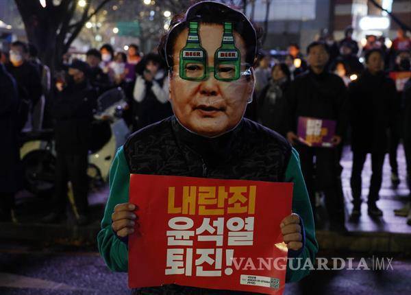 $!Un manifestante con una máscara que muestra el rostro del presidente Yoon Suk Yeol sostiene un cartel que dice: “¡Yoon Suk Yeol, dimite por traición!”.