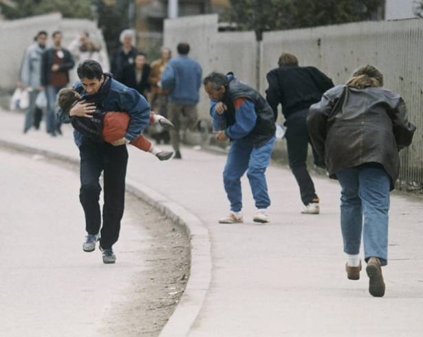 Un hombre acuna a su hijo mientras la gente pasa corriendo por uno de los peores lugares para los francotiradores en Sarajevo en abril de 1993.