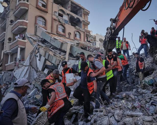 Equipos de defensa civil palestinos cargan con un cuerpo rescatado de entre los escombros de un edificio derrumbado en el que vivían familias palestinas desplazadas.
