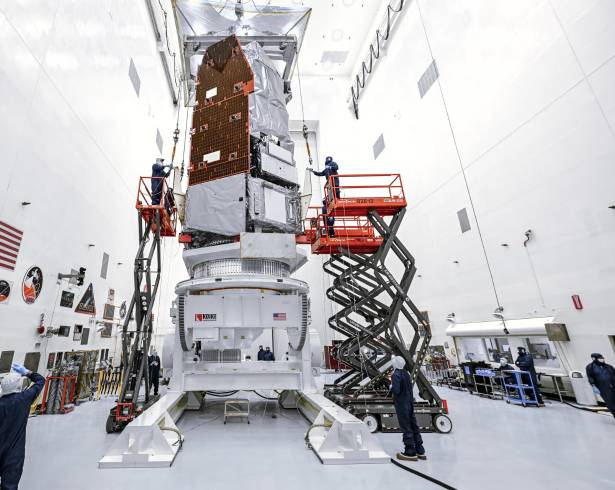 Técnicos e ingenieros de la Instalación de Procesamiento de Cargas Útiles Peligrosas utilizando una grúa para elevar el telescopio espacial Nancy Grace Roman en una plataforma de trabajo en Florida.