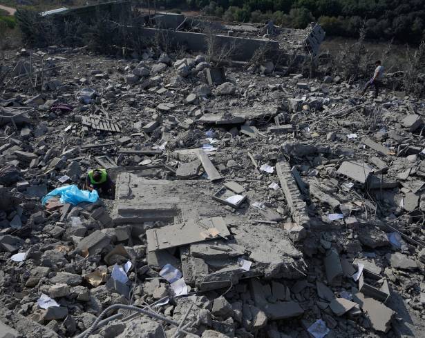 Un rescatista, a la izquierda, busca víctimas bajo los escombros de una casa que fue alcanzada por un ataque aéreo israelí en la población de Ansar.