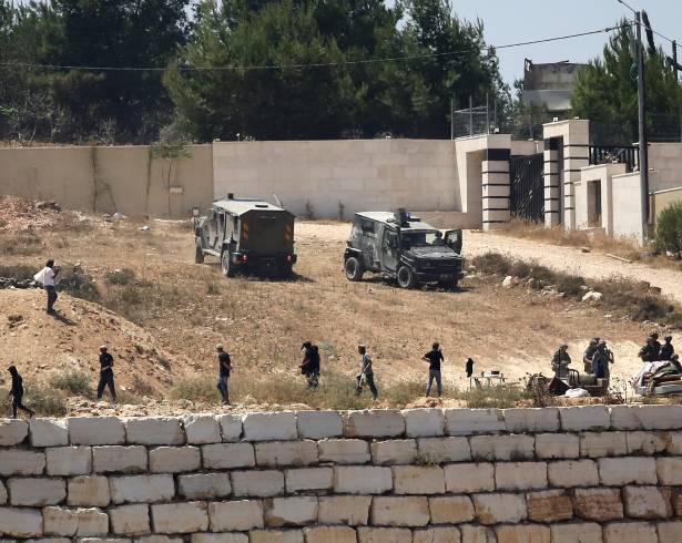 Soldados israelíes hacen guardia junto a colonos frente a viviendas palestinas que estos bloquearon en la localidad de Qusra, al sur de Nablus, en la ocupada Cisjordania, el 12 de agosto de 2026.