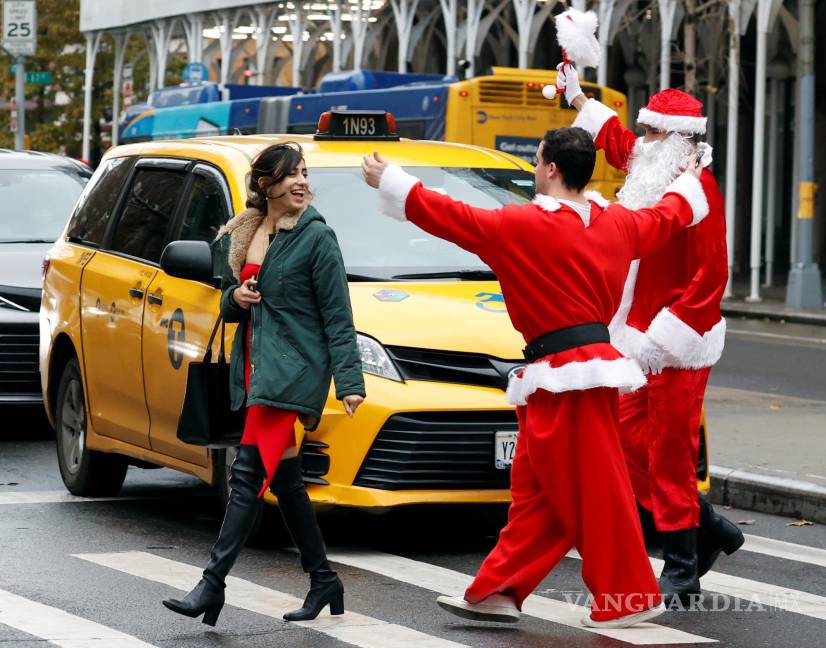 $!Personas vestidas con trajes de Papá Noel junto a un taxi de la ciudad de Nueva York. EFE/EPA/Jason Szenes