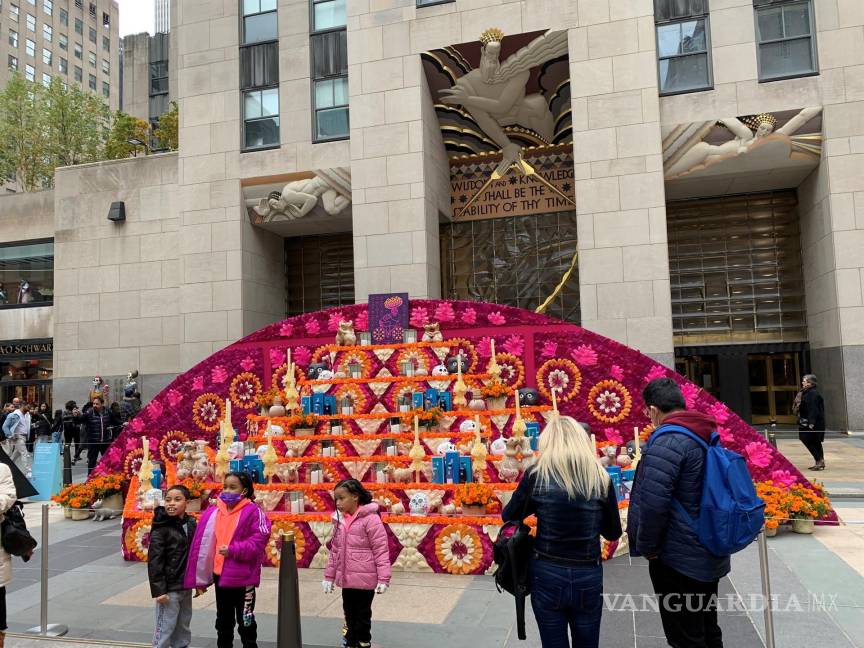 $!Unas personas se toman fotos frente al enorme altar del Día de los Muertos, decorado con pétalos de vibrantes colores, calaveras, velas, botellas de tequila, vasijas y perros de la raza xoloitzcuintle, instalado en una de las plazas del Rockefeller Center en Nueva York. EFE/Helen Cook