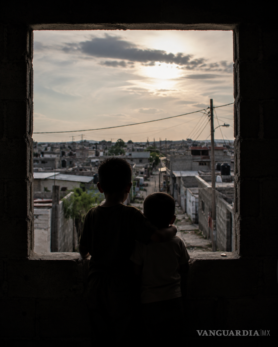 $!Dos menores observan la colonia desde una ventana de la vivienda familiar. En el caso narrado, las consecuencias no se limitan a la experiencia de la mujer: también atraviesan la infancia y las condiciones en las que sus hijos imaginan el futuro.