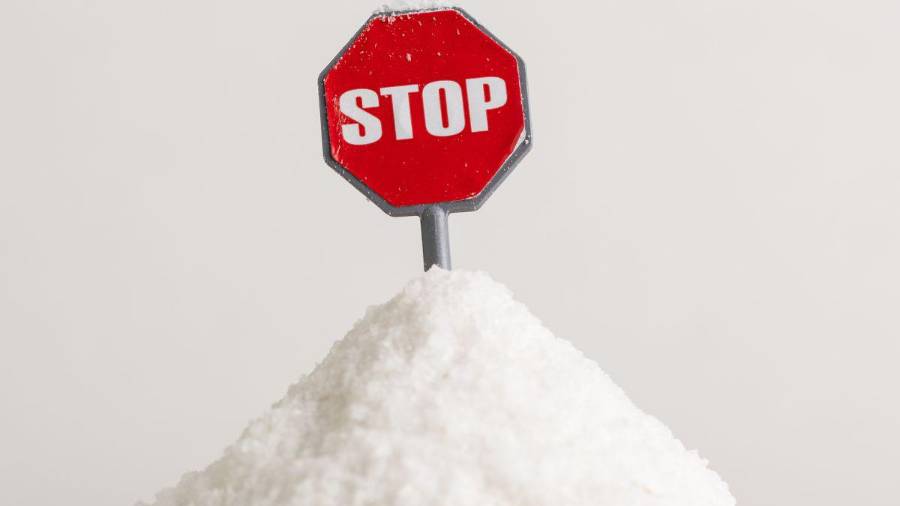 Una señal de alto sobre una montaña de sal recuerda que moderar el consumo de sodio es clave para cuidar el corazón y prevenir la hipertensión.