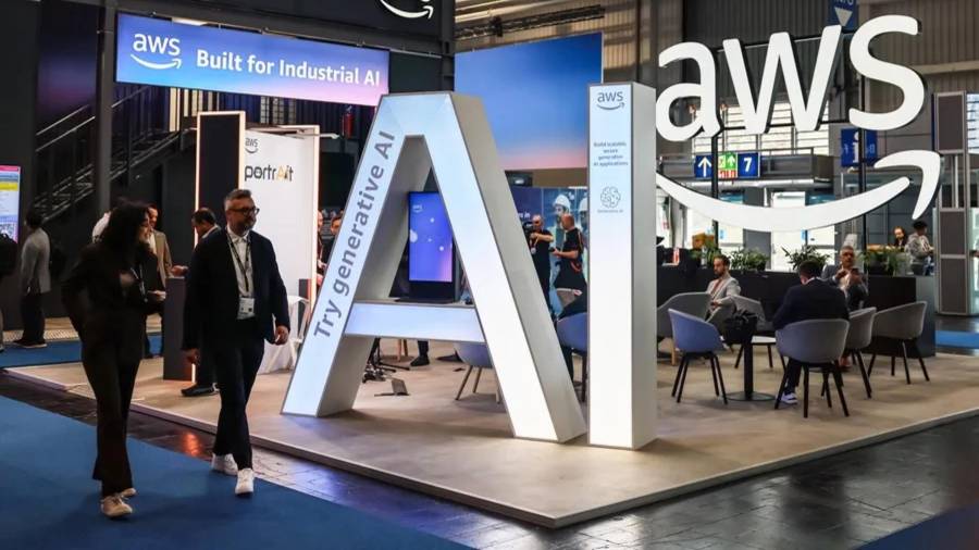 Fotografía de archivo de dos visitantes pasando junto al stand de Amazon Web Services (AWS).