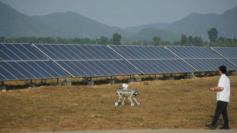 Un trabajador controla un perro robótico cerca de paneles solares en una planta de energía fotovoltaica operada por Huadian (Beijing) New Energy Development Co. Ltd. en Pekín.