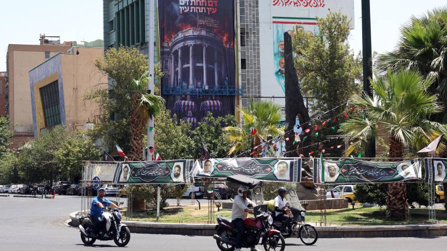 Iraníes pasan junto a una valla publicitaria antiestadounidense con imágenes de Donald Trump y su familia sobre ataúdes, acompañada de una frase que dice “Sangre por sangre”, en la Plaza Palestina en Teherán, Irán.