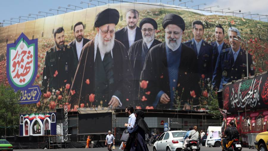 Ciudadanos iraníes caminan frente a una gran valla publicitaria con imágenes del difunto líder supremo iraní, el ayatolá Ali Jamenei, y del difunto presidente iraní, Ebrahim Raisi, en la plaza Enghelab de Teherán.