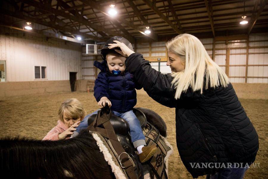 $!Louann Gross (i), y Tammy Cunningham (d) ayudan al hijo de Tammy, Calum, a subirse a un caballo en una granja y guardería en Kokomo, Indiana.