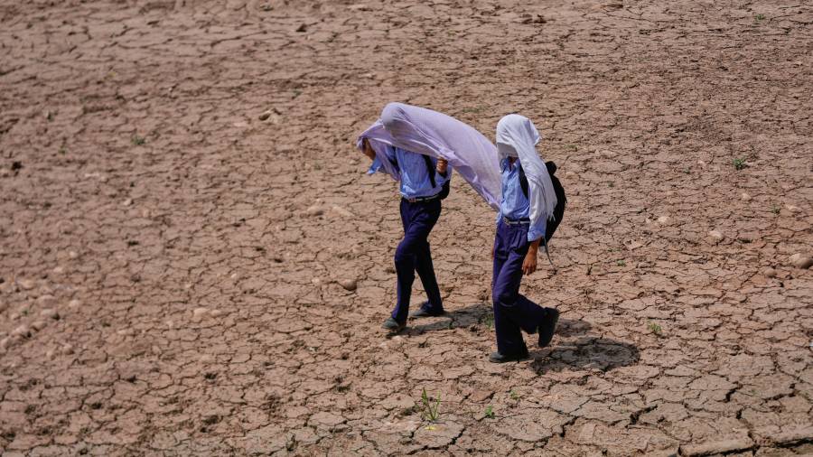 Niños en edad escolar se cubren la cabeza con toallas de algodón para protegerse del calor abrasador de la tarde mientras caminan por un campo reseco en las afueras de Jammu, India,