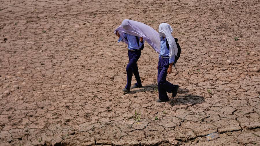 Niños en edad escolar se cubren la cabeza con toallas de algodón para protegerse del calor abrasador de la tarde mientras caminan por un campo reseco en las afueras de Jammu, India,
