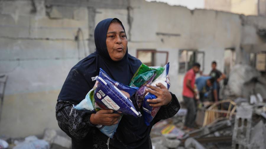 Una mujer palestina carga bolsas de azúcar, todo lo que pudo rescatar de su casa después de que fuera destruida en un ataque israelí nocturno, en Nuseirat, en el centro de la Franja de Gaza.