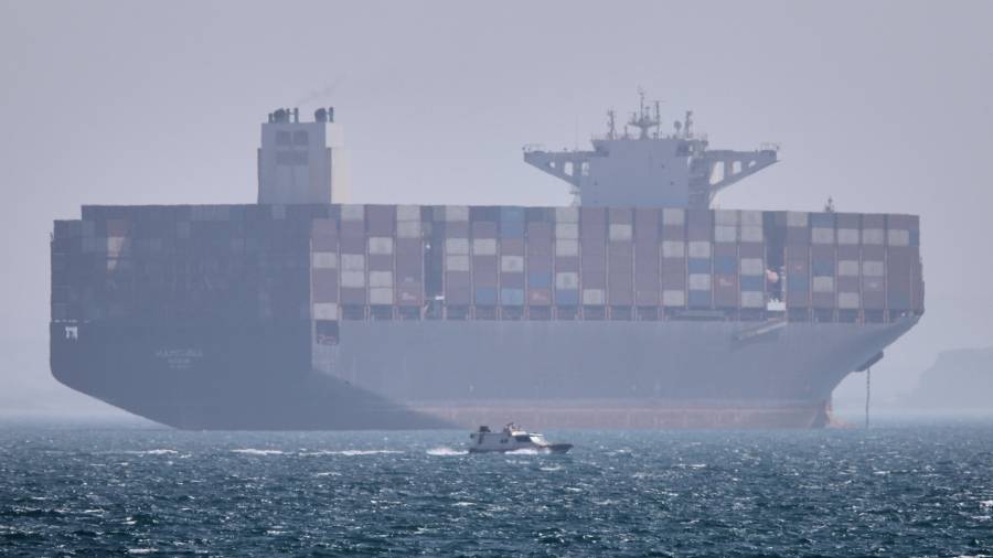 Un barco portacontenedores se ve fondeado mientras una lancha pasa por delante en el estrecho de Ormuz, cerca de Bandar Abbas, Irán.