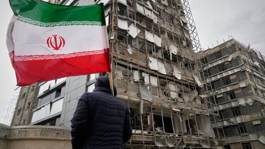 Un hombre con una bandera iraní observa la fachada dañada de Hospital Gandhi, alcanzado durante una campaña de bombardeos estadounidenses e israelíes, en Teheránm Irán, el lunes 2 de marzo de 2026.