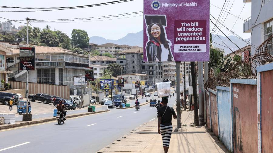 Una mujer pasa junto a un cartel que promociona el proyecto de ley de Maternidad Segura, en Wilkinson Road, Freetown, Sierra Leone, el 12 de marzo de 2025.